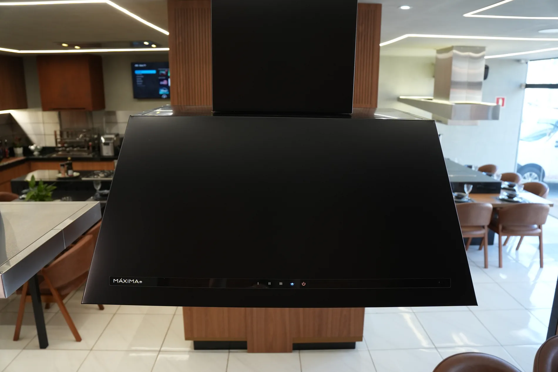 Coifa Máxima Delicatta preta instalada sobre ilha de cocção no showroom