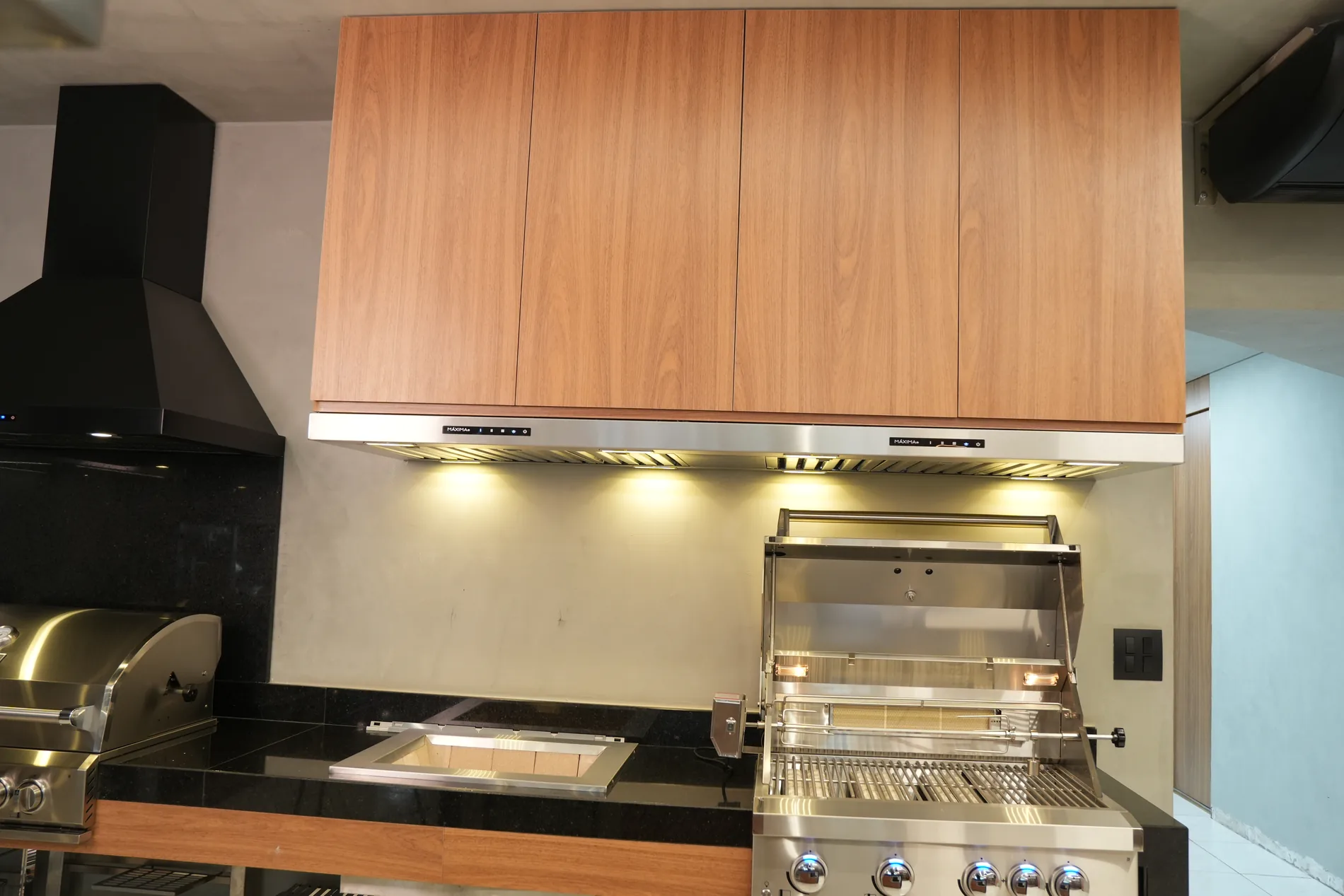 Coifa Máxima Integra embutida na marcenaria, sobre grill e cooktop da área gourmet